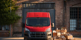 Roter Kurier-Van vor Paketboxen in einem Industriehof, warmes Tageslicht