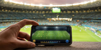 Smartphone auf einer Stadionbrüstung mit Fußball-App vor einem beleuchteten Stadion