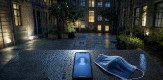 Anonymes Smartphone auf nasser Steinbank vor Berliner Hausfassade, daneben eine Maske im kühlen Licht