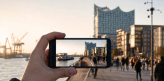 Hand hält Smartphone mit Zeitraffer einer Hamburger Uferpromenade im Morgenlicht