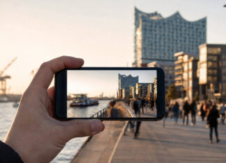 Hand hält Smartphone mit Zeitraffer einer Hamburger Uferpromenade im Morgenlicht