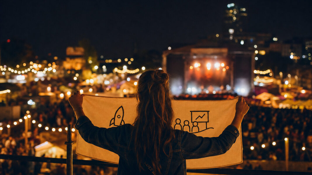 Person von hinten mit Banner auf beleuchtetem Festivalgelände bei Abendlicht