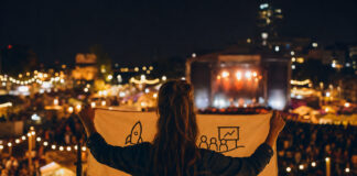 Person von hinten mit Banner auf beleuchtetem Festivalgelände bei Abendlicht