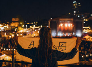 Person von hinten mit Banner auf beleuchtetem Festivalgelände bei Abendlicht