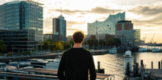 Gründer blickt auf Hamburgs Hafen und moderne Startup-Gebäude im warmen Nachmittagslicht.