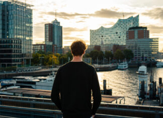 Gründer blickt auf Hamburgs Hafen und moderne Startup-Gebäude im warmen Nachmittagslicht.