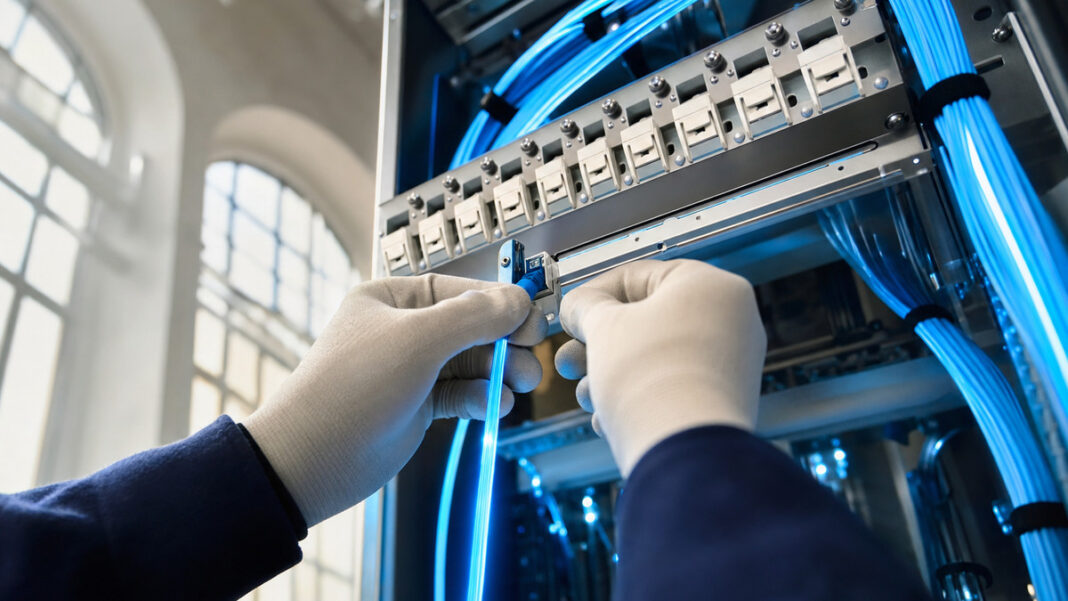 Globale Internetnutzung Hände verbinden ein blaues Glasfaserkabel in einer hellen Verteilanlage.