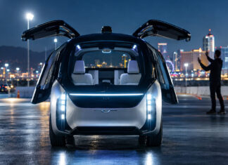 Autonomes Konzeptauto auf beleuchteter Teststrecke bei Nacht, eine Hand zeigt Gesten im Hintergrund