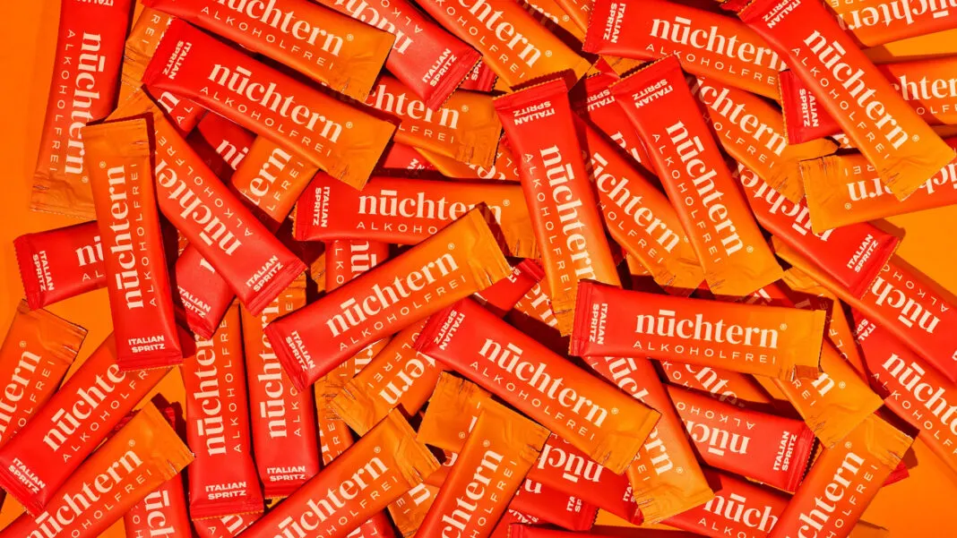 Viele Portionsbeutel des alkoholfreien Italian Spritz von nüchtern liegen auf orangefarbenem Grund