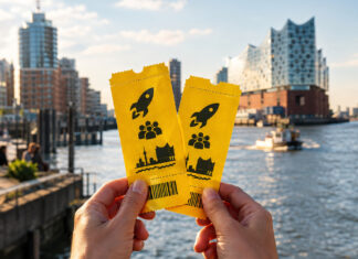 Hände halten zwei Tickets vor der Hamburger HafenCity im warmen Licht