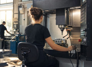 Frau an CNC-Fräse in moderner Werkhalle, im Hintergrund eine zweite Person als Silhouette