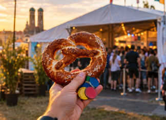 Hand mit Brezn und bunten Chips vor Festivalzelt mit wartenden Menschen