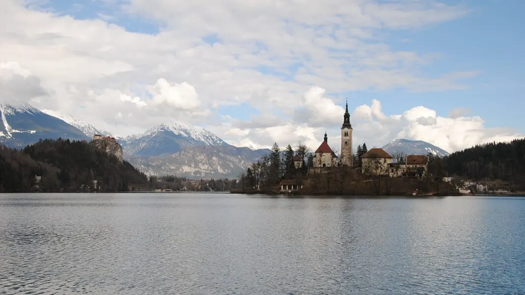 Insel mit Kirchturm im See von Bled, im Hintergrund schneebedeckte Gipfel der Julischen Alpen