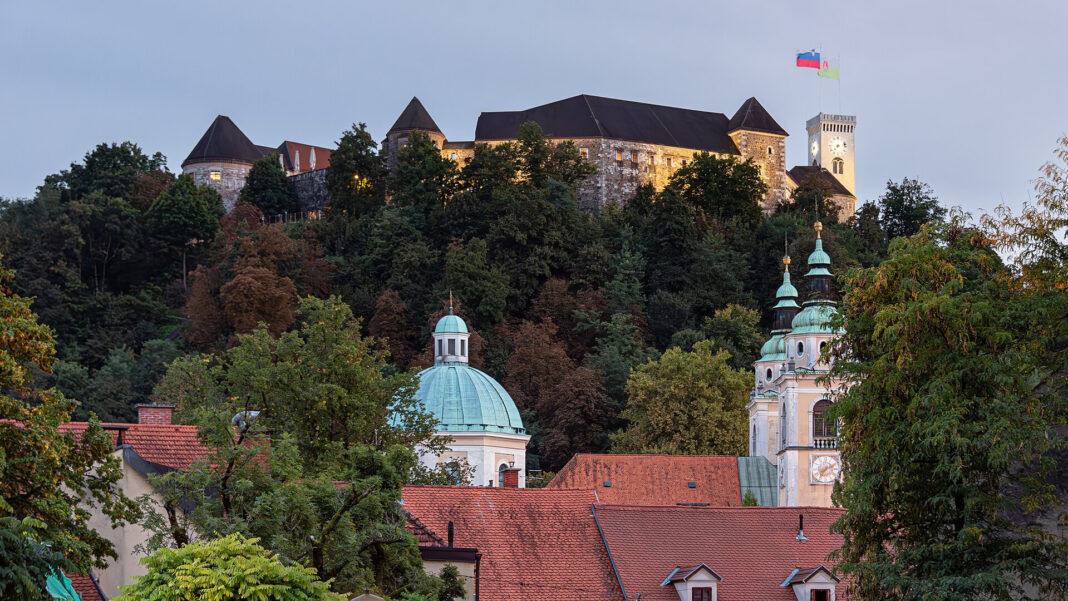 Burg von Ljubljana über bewaldetem Hang, darunter die Kuppel und die Türme der Altstadt