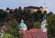 Burg von Ljubljana über bewaldetem Hang, darunter die Kuppel und die Türme der Altstadt