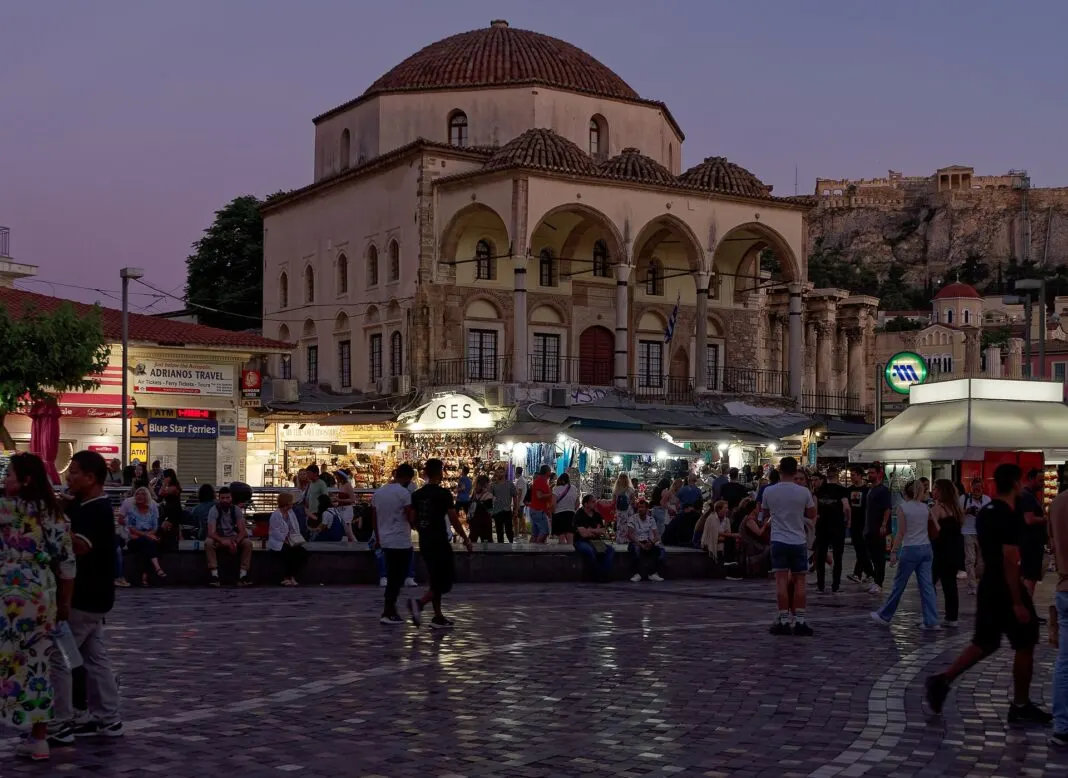 Abendlicher Monastiraki-Platz in Athen mit Geschäften, Passanten und der Akropolis im Hintergrund