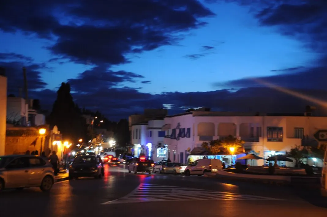 Belebte Straße in Sidi Bou Saïd in der blauen Stunde, mit beleuchteten Häusern und Autos