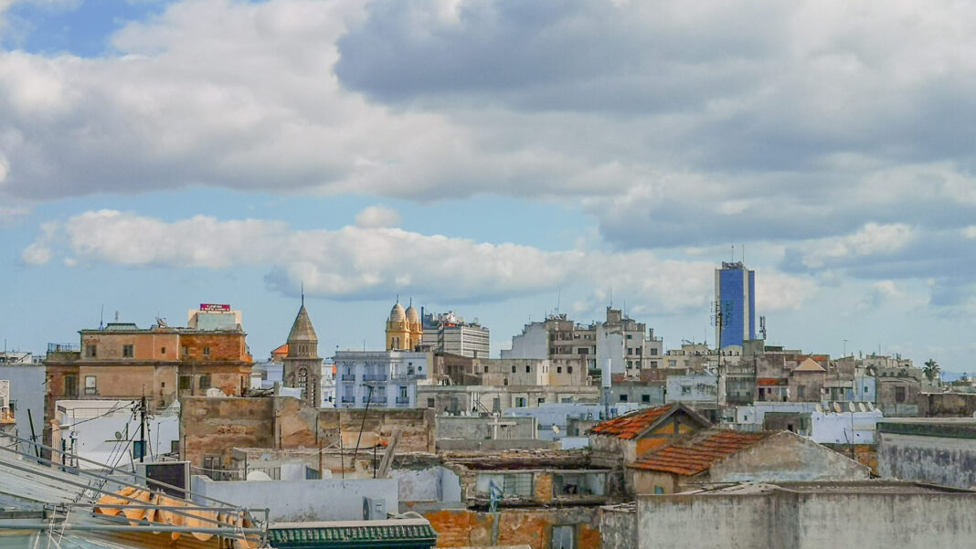 Auswandern nach Tunesien: Aufenthalt, Kosten und Steuern Blick über die Dächer von Tunis mit Kirchtürmen und einem blauen Hochhaus im Hintergrund