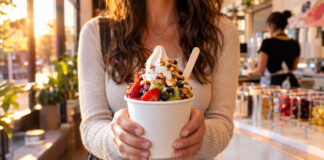 Person hält einen Becher Frozen Yogurt mit Toppings in einer hellen Eisdiele