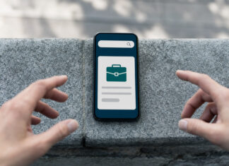 Smartphone mit reduzierter Jobsuche auf Steinmauer, Hände greifen danach im Tageslicht
