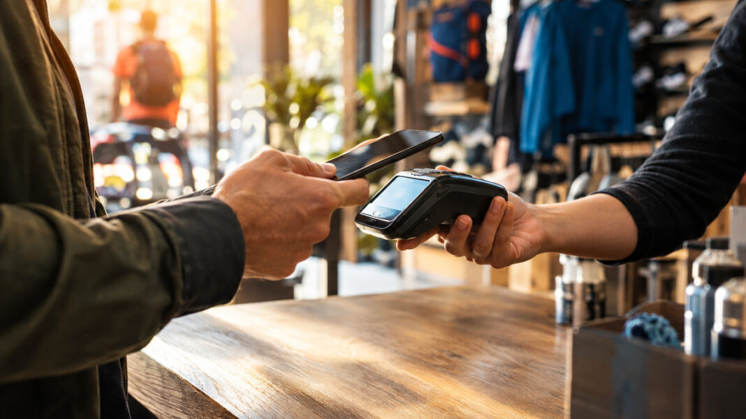 Kunde bezahlt im Sportgeschäft kontaktlos mit Smartphone am Kartenterminal.