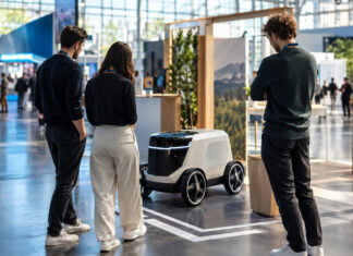 Gründerteam am Messestand mit Modellauto auf Startlinie in einer hellen Messehalle