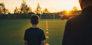 Fußballer von hinten am Trainingsplatz neben Hütchen im Abendlicht