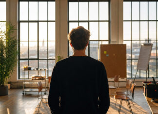 Gruenderfreunde.de – Der erste Monat, Neuigkeiten aus dem Betahaus Hamburg. Ein Resümee von Dennis Weidner Junger Gründer von hinten vor einer Fensterfront im Betahaus, mit kleinem Workshop-Bereich und Morgenlicht.
