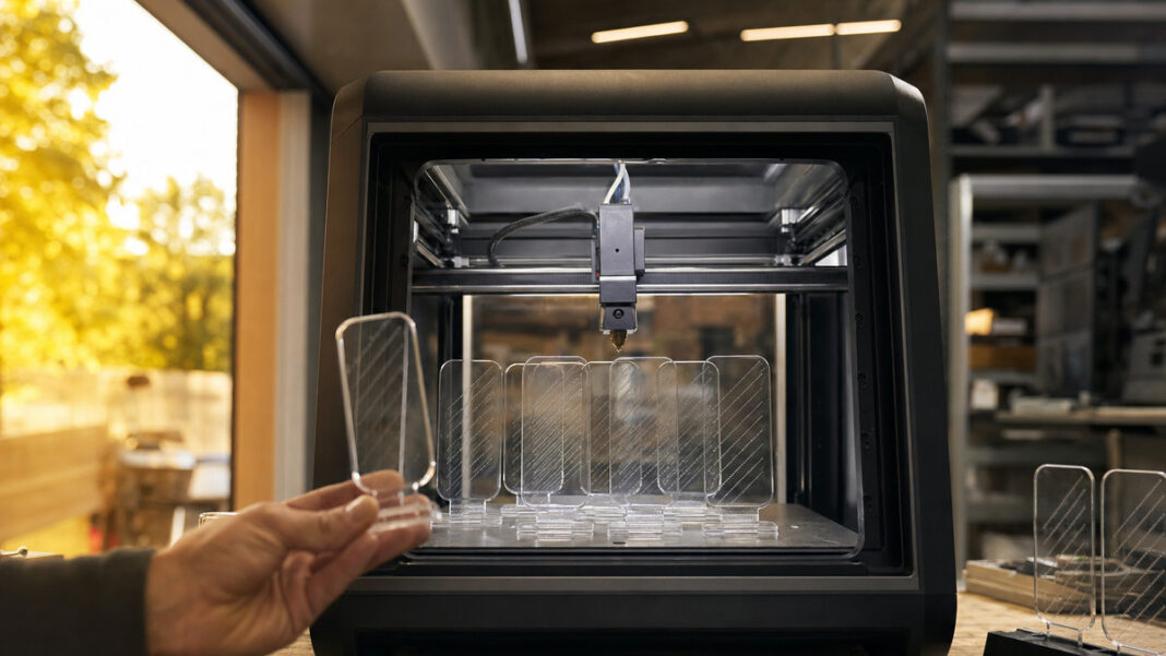 Digitale Werbung in der Manufaktur 3D-Drucker fertigt transparente Werbe-Displays, eine Hand prüft die Druckprobe im Seitenlicht.