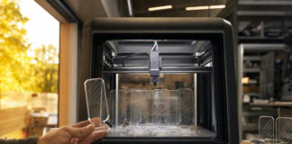 3D-Drucker fertigt transparente Werbe-Displays, eine Hand prüft die Druckprobe im Seitenlicht.