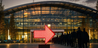 Roter LED-Pfeil vor einer modernen Eventhalle in München, davor Silhouetten von Konferenzbesuchern