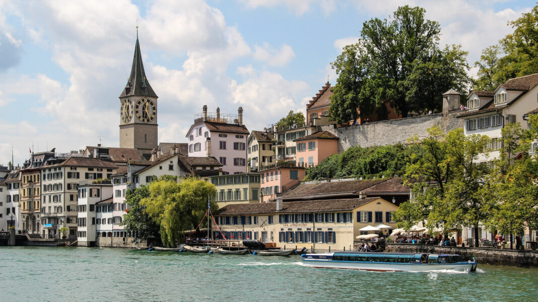 Auswandern nach Zürich: Kosten, Anmeldung und Gründung Altstadthäuser und der Turm von Sankt Peter am Ufer der Limmat in Zürich