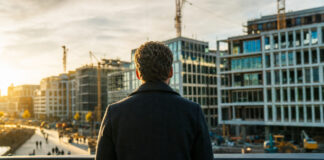 Gründer von hinten blickt auf ein modernes Viertel mit Baustellen und Aufbruchsstimmung im Morgenlicht.