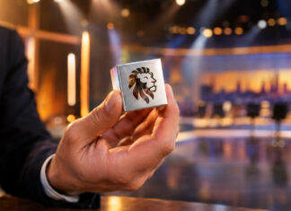 Hand hält silbernen Würfel mit Löwenkopf in einem Fernseh-Studio