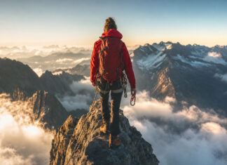 Bergsteigerin am Grat mit Karabiner, Wolken unter ihr und warmem Seitenlicht