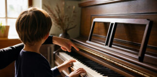 Kind spielt am Klavier, eine Hand zeigt unterstützend auf die Tasten, warmes Fensterlicht