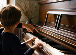 Kind spielt am Klavier, eine Hand zeigt unterstützend auf die Tasten, warmes Fensterlicht