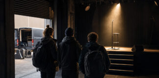 Leerer Musikclub mit beleuchteter Bühne, Mikrofon und Barhocker, Gründerteam von hinten im Eingang
