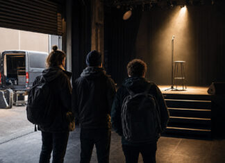 Leerer Musikclub mit beleuchteter Bühne, Mikrofon und Barhocker, Gründerteam von hinten im Eingang