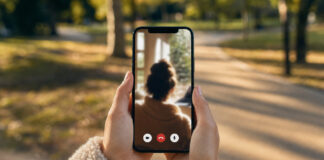 Hände halten ein Smartphone mit Videoanruf vor einem leeren Parkweg im Nachmittagslicht