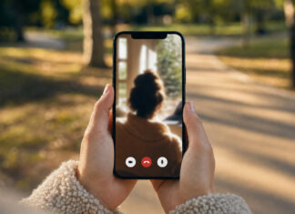 Hände halten ein Smartphone mit Videoanruf vor einem leeren Parkweg im Nachmittagslicht