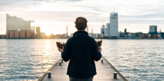 Gründer hält ein kleines Holzschiff auf einer Hafenpromenade im Morgenlicht.