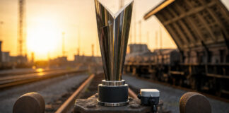 Award-Pokal auf Eisenbahnkupplung mit IoT-Sensor im Gleisbereich, warmes Licht