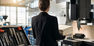 Unternehmerin von hinten in einer Werkstatt mit Zertifikatspaket und Fräsmaschine im Tageslicht