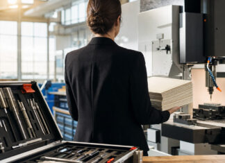 Unternehmerin von hinten in einer Werkstatt mit Zertifikatspaket und Fräsmaschine im Tageslicht