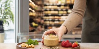 Hand platziert ein Glas mit neuem Aufstrich auf einer Probierstation im Supermarkt.