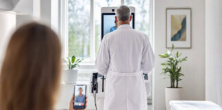 Arzt in Praxis mit Telemedizin-Terminal, Patientin per Smartphone zugeschaltet