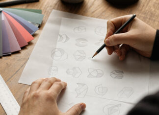 Ein Startup-Logo mit knappem Budget entwerfen Hände skizzieren mehrere Logo-Entwürfe auf Transparentpapier neben Farbfächern.