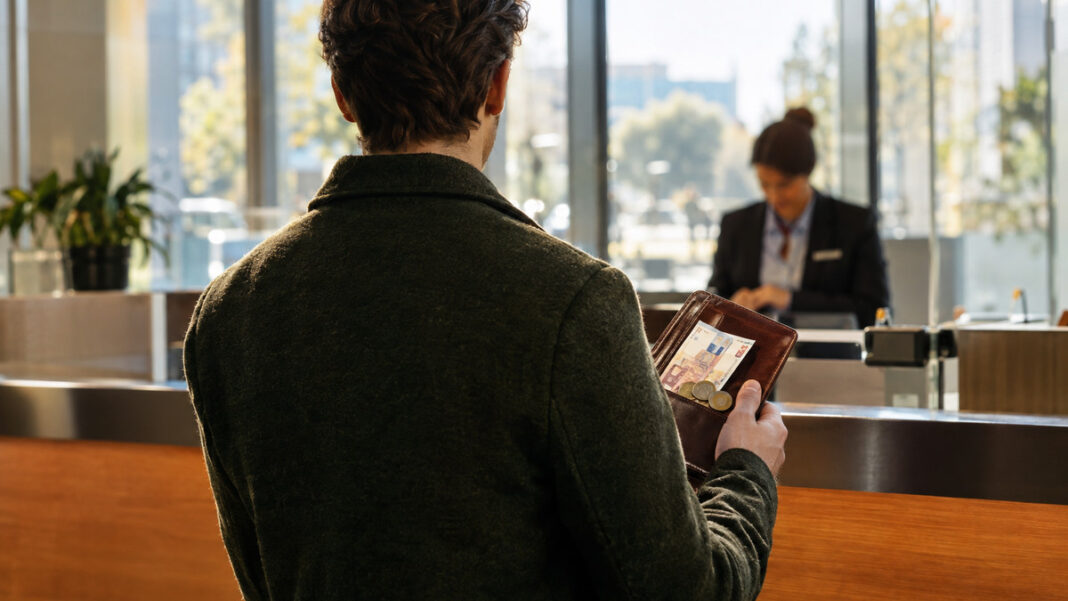 Finanzierung ohne Investor am Bankschalter Person mit Ledermappe, Geldscheinen und Muenzstuecken am Bankschalter im Tageslicht
