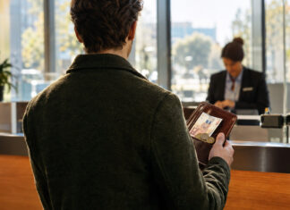 Finanzierung ohne Investor – Welche Möglichkeiten haben Gründer*innen? Person mit Ledermappe, Geldscheinen und Muenzstuecken am Bankschalter im Tageslicht